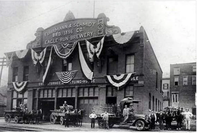 Historic Eagle Run Brewery building with bunting, workers, wagons, and horses