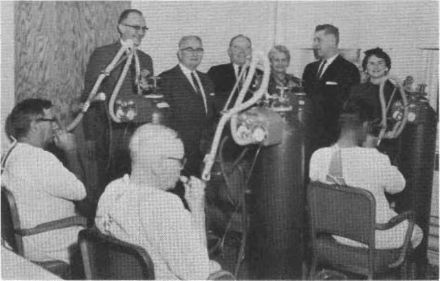 Black-and-white photograph of people gathered around respiratory equipment in a hospital clinic