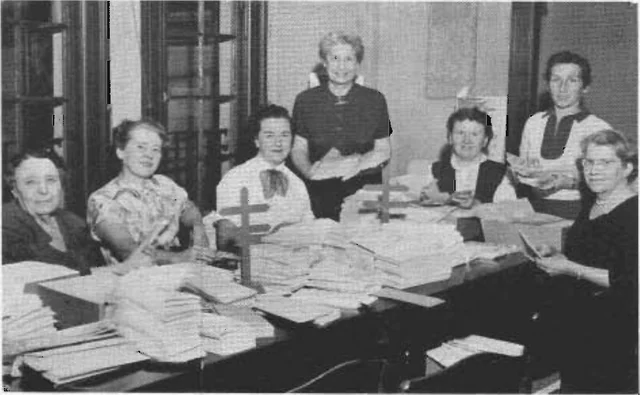 Black-and-white photograph of seven volunteers around a table covered with Christmas Seal Drive materials