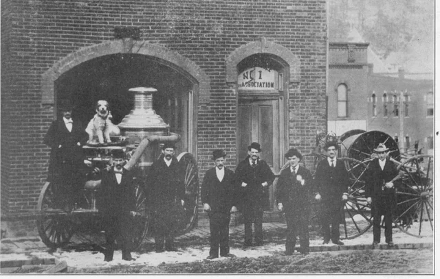 Historic black-and-white group photograph outside the Independence Fire Association house with a horse-drawn steam fire engine